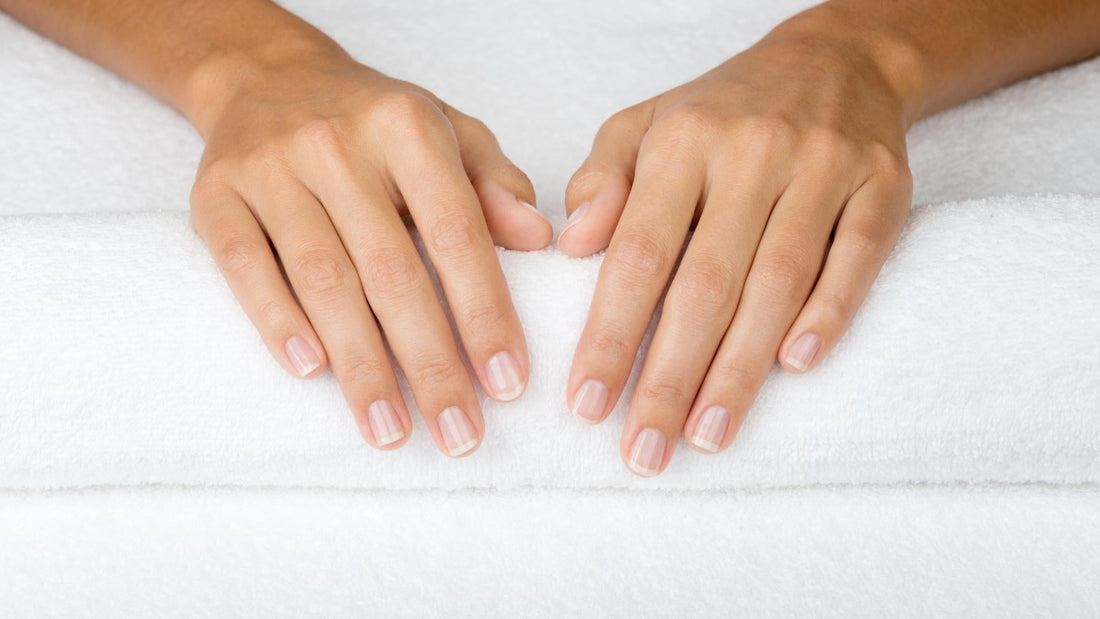 Manos con uñas blancas bien cuidadas sobre una toalla