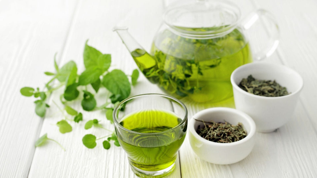 Té verde en una taza con hojas frescas sobre una mesa de madera blanca, con el lema "Del laboratorio a tu taza".