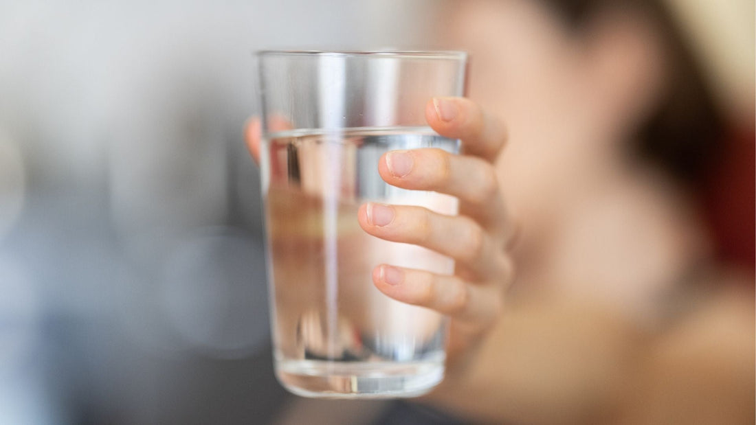 Mujer sosteniendo un vaso de agua, simbolizando la importancia de mantenerse hidratada.