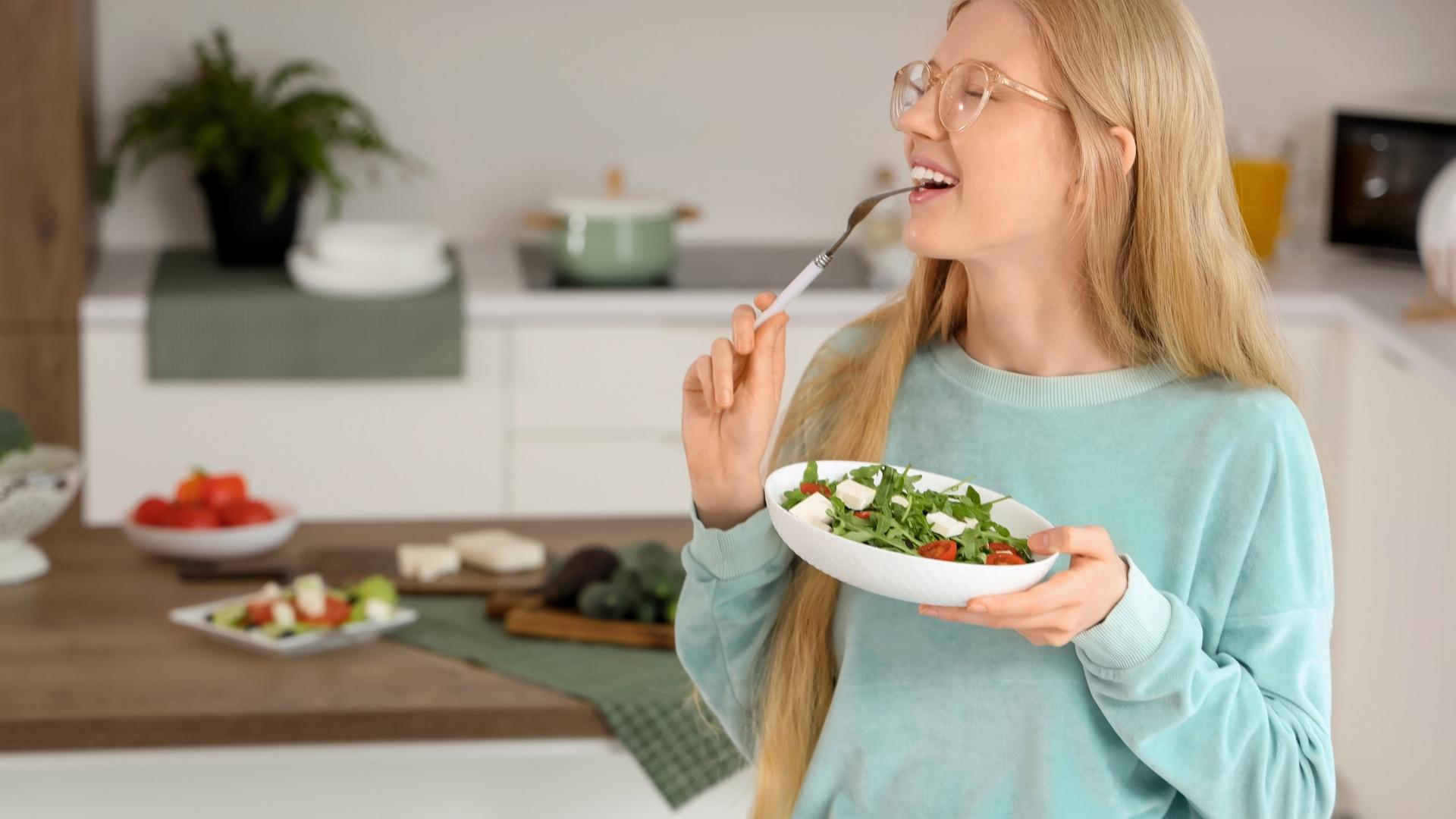 Mujer comiendo una ensalada en la cocina.