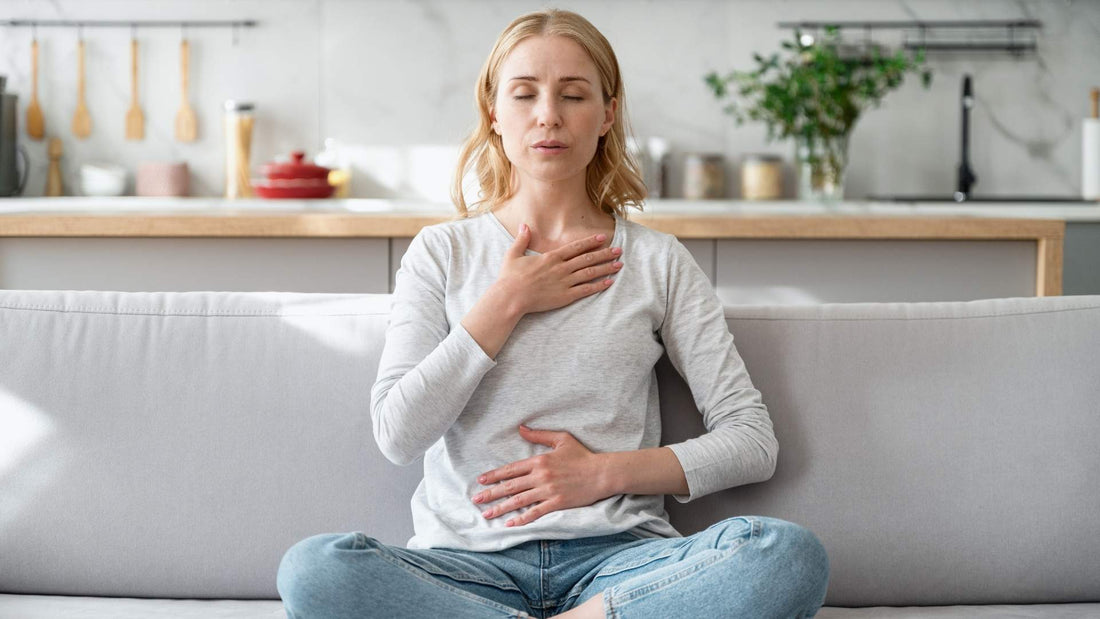 Mujer sentada en un sofá, con las manos sobre el estómago, reflexionando sobre rituales de transformación.