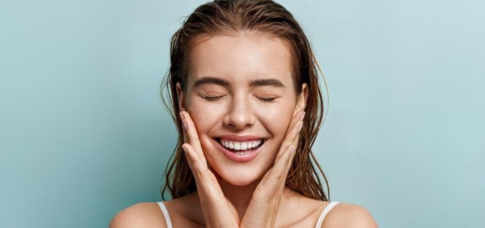 Mujer sonriente tocándose la cara, mostrando una expresión de alegría y satisfacción.