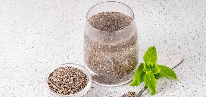 Semillas de chía en un plato junto a un vaso de agua transparente.